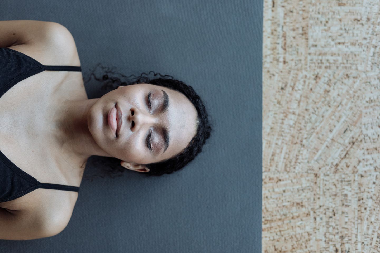 A serene portrait of a woman with curly hair lying on a yoga mat indoors, exuding calmness.