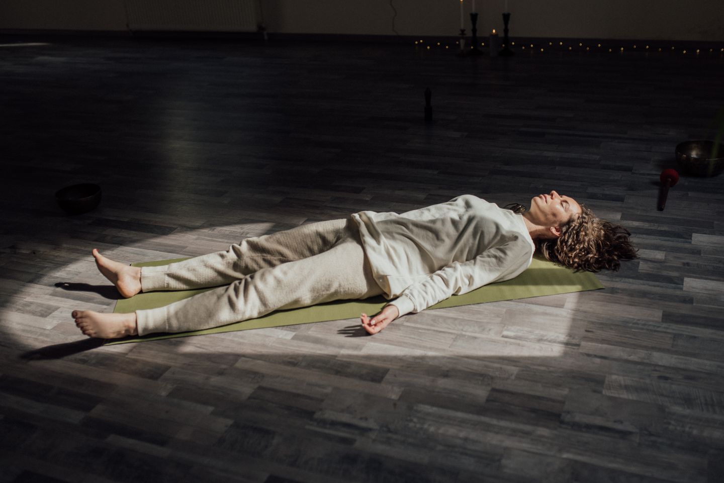 Woman lying on a yoga mat indoors, meditating and relaxing in a calm setting.